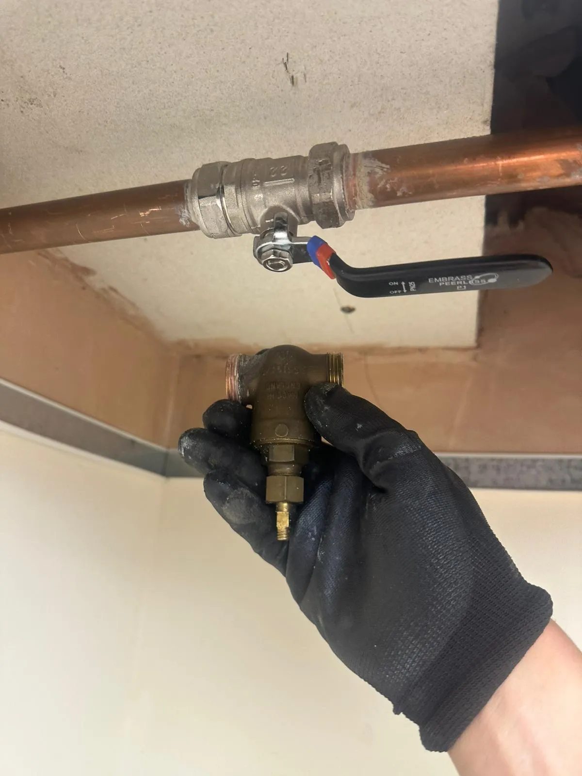 A gloved hand holds a brass valve near copper pipes in a renovation setting, showcasing plumbing work.