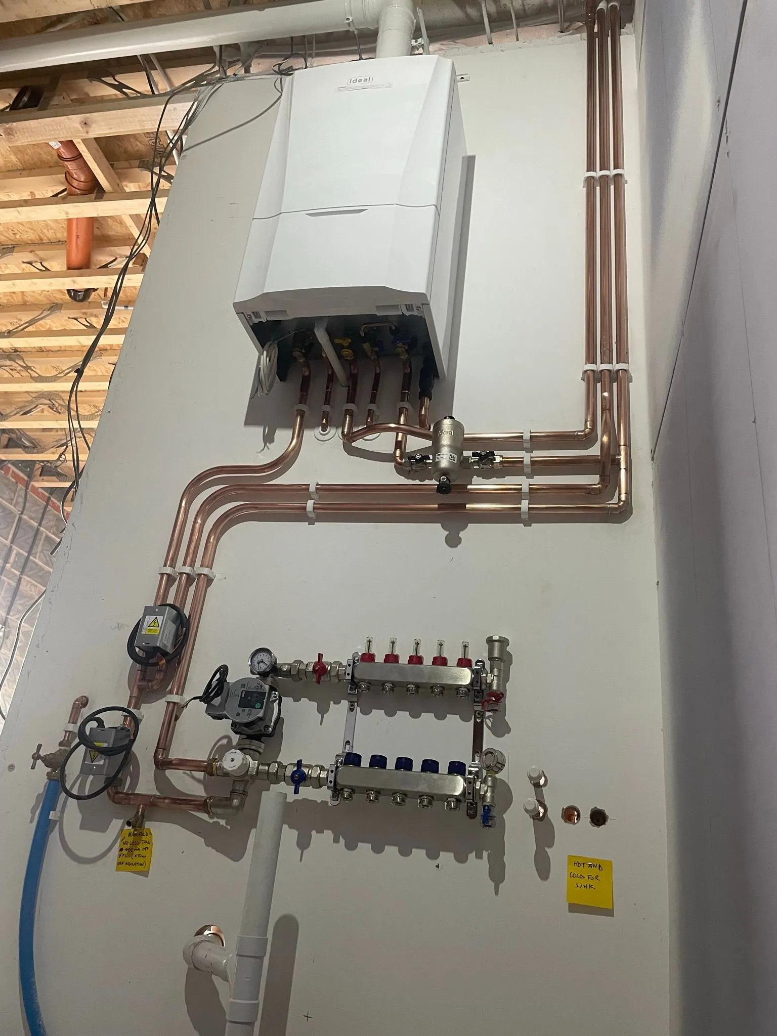 A wall-mounted boiler with copper piping and valves. Additional components include water meters and labeled connections for a heating system.
