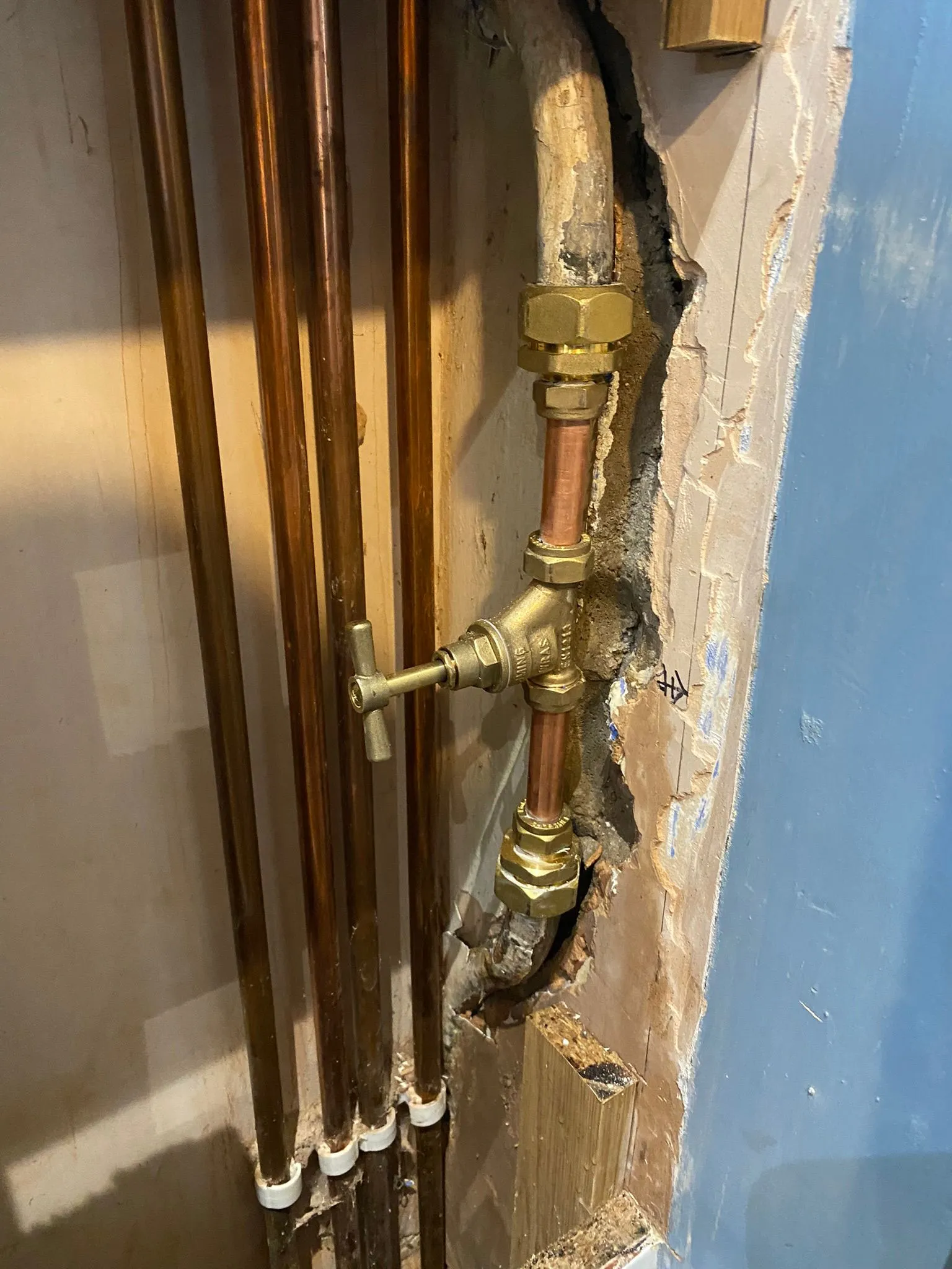 Exposed plumbing pipes with a brass shut-off valve in a wall, showing wear and partially damaged drywall.
