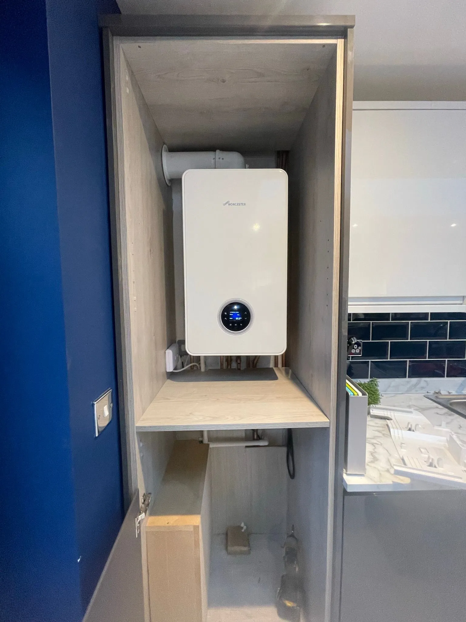 A modern wall-mounted boiler in a wooden enclosure, featuring a digital display, situated in a contemporary kitchen setting.
