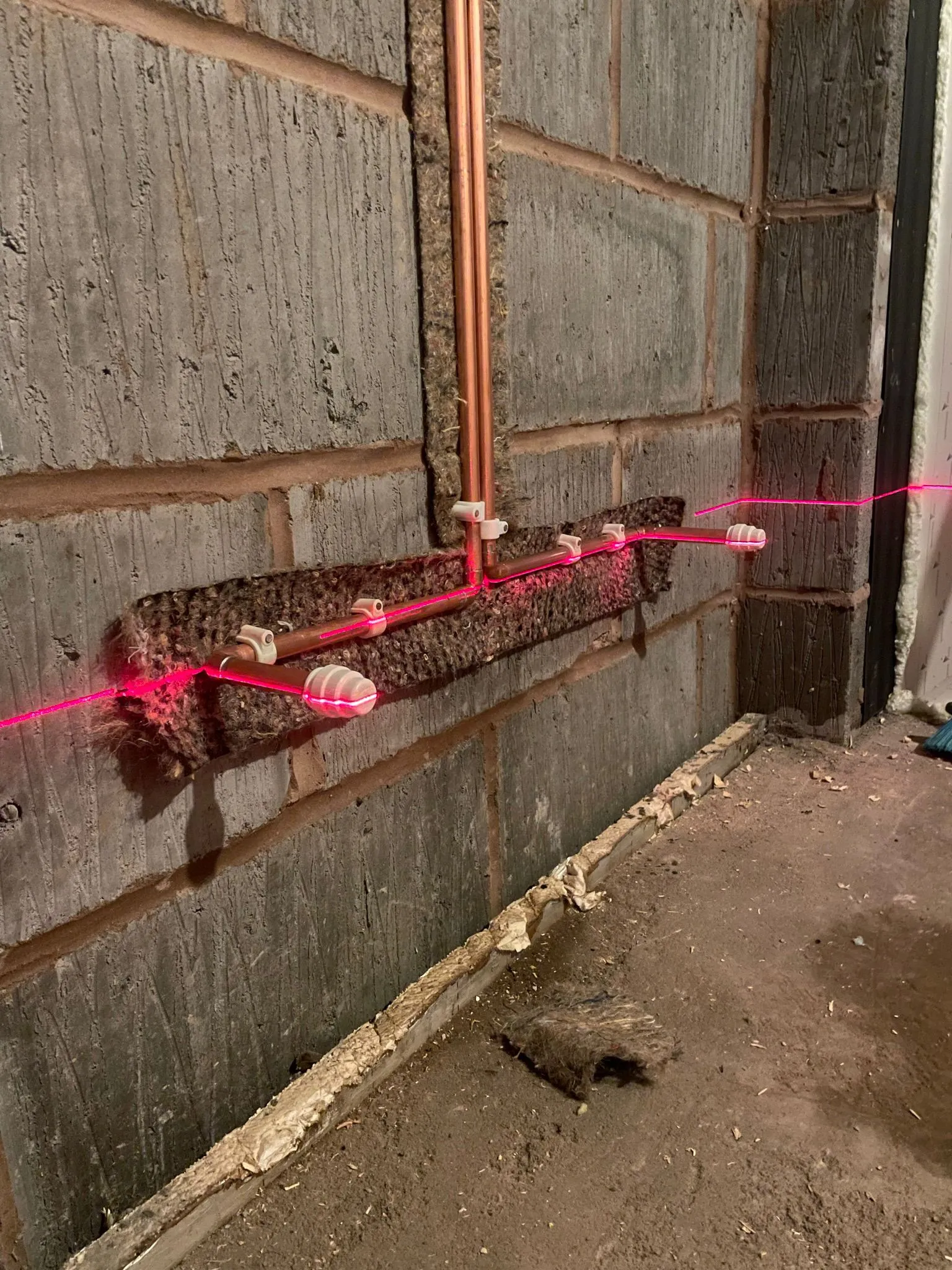 Copper pipes mounted on a wall with laser levels, demonstrating plumbing installation setup in a construction area.