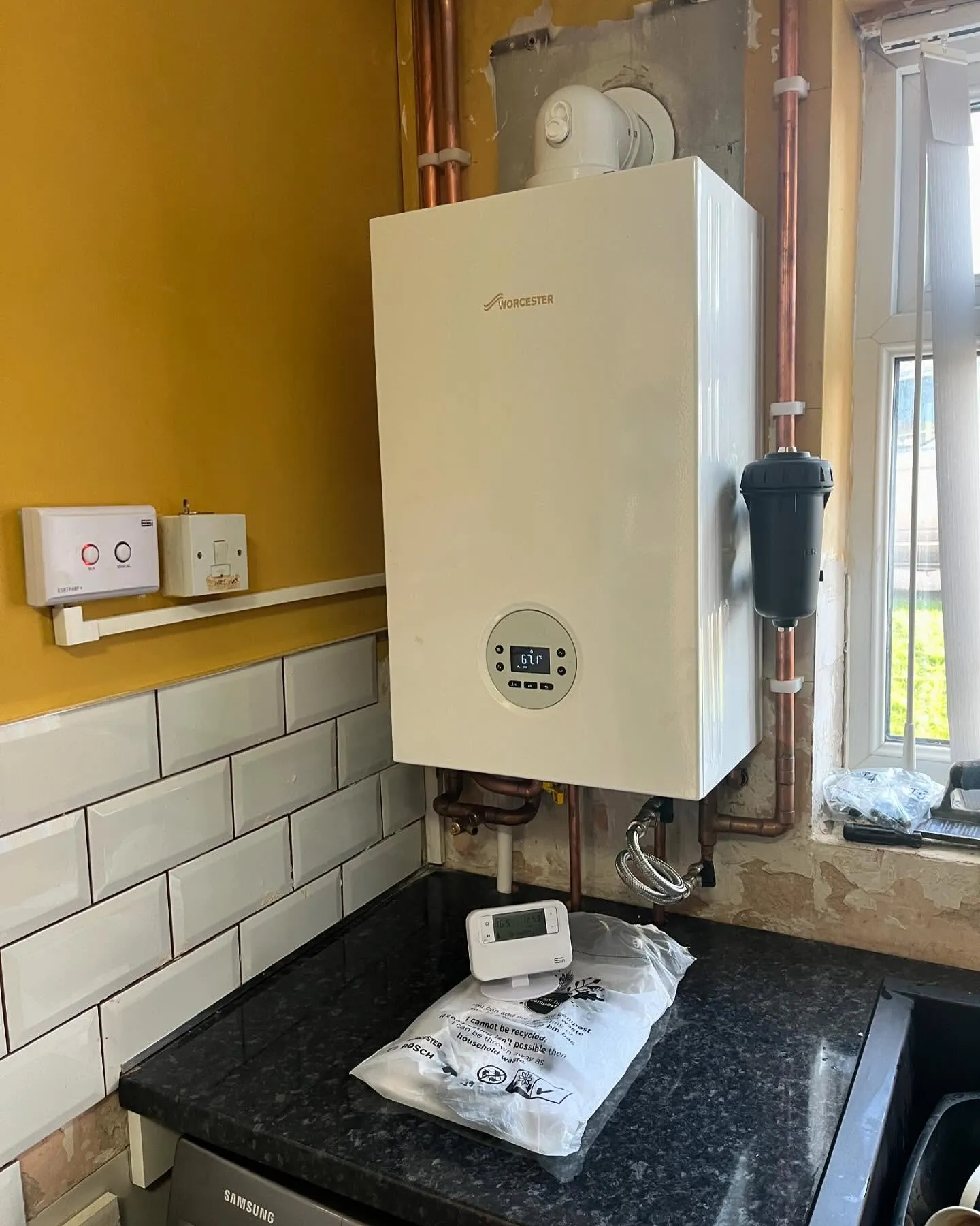 Modern boiler installation in a kitchen with copper pipes, digital display, and a thermostat on a black countertop.