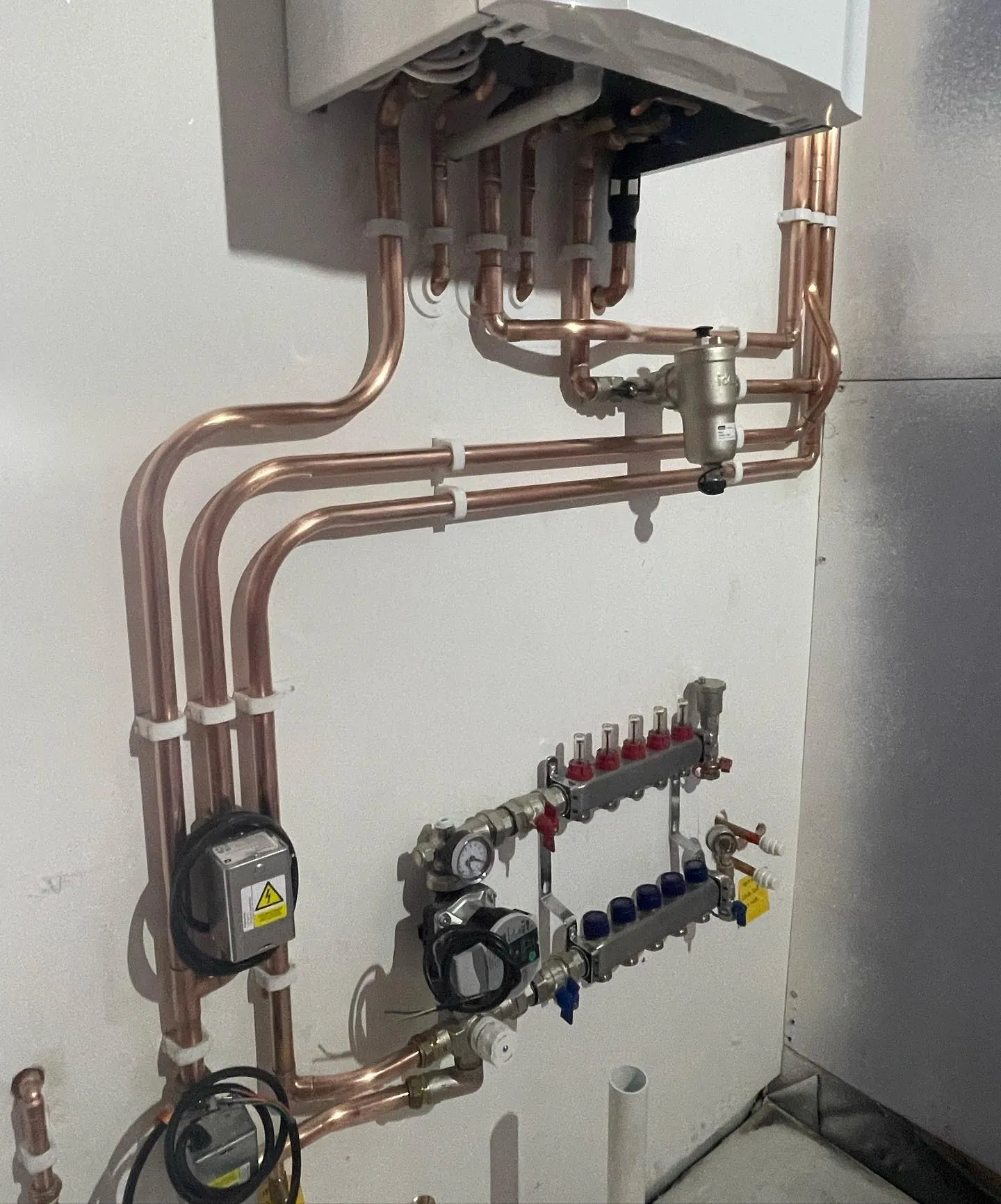 Copper piping and a control panel installation on a wall, showcasing valves, gauges, and a water heater connection.