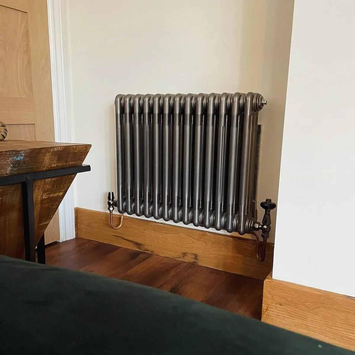 A vintage-style metal radiator sits against a wall, next to a wooden table in a cozy interior setting.