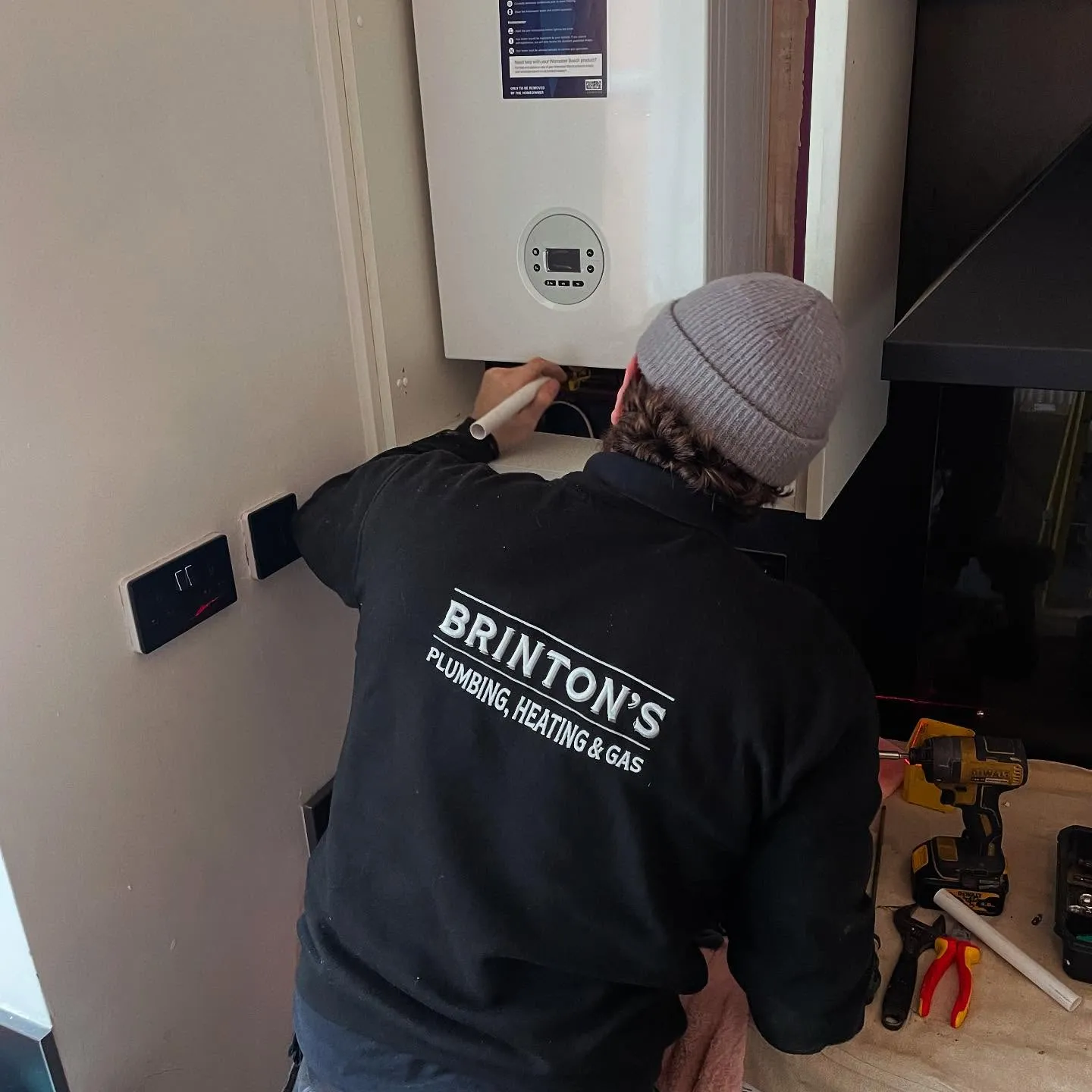 A technician in a black jacket works on a white gas boiler, surrounded by tools on a cloth.